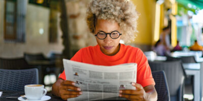 A woman reading a newspaper in a café.