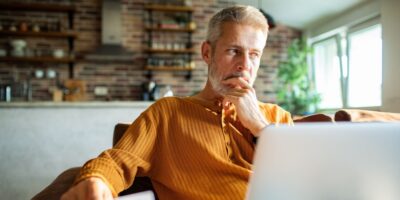 A man in his 50s thinking while using a laptop