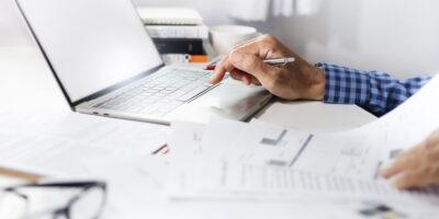 Man’s hands at a laptop, with financial paperwork