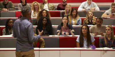 Back view of a man presenting to students at a lecture theatre