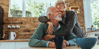 An older couple smiling and hugging at the dinner table.